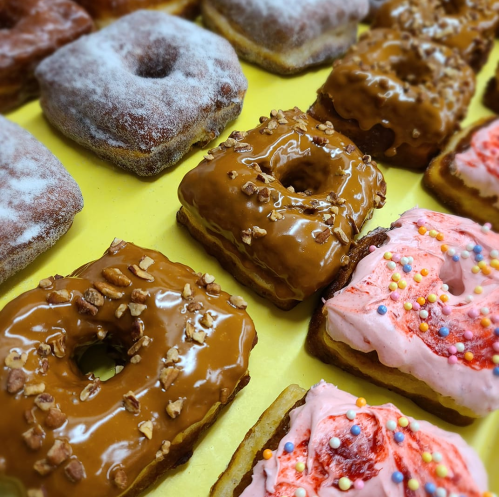 A variety of donuts, including glazed, frosted, and topped with nuts, arranged on a yellow background.