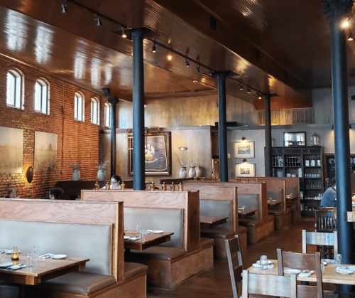 Interior of a restaurant featuring wooden booths, brick walls, and warm lighting, with diners in the background.