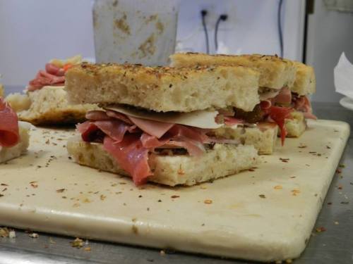 A close-up of a sandwich stacked with various meats on a rustic bread, resting on a cutting board.