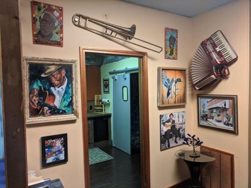A wall adorned with various framed artworks, including musical instruments and portraits, leading to a doorway.