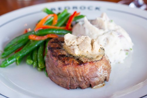 A grilled steak topped with creamy sauce, served with mashed potatoes and sautéed green beans and peppers.