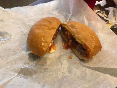 A split sandwich on parchment paper, filled with meat, diced onions, and sauce, with a soft bun.