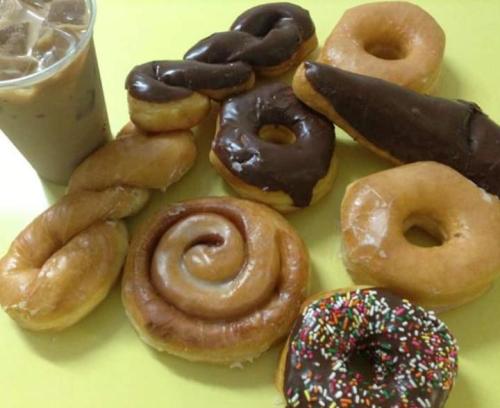 A variety of donuts, including chocolate-covered, glazed, and a sprinkle donut, alongside a cup of iced coffee.