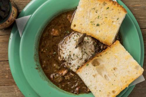 A bowl of stew with rice, garnished with parsley, served with two slices of toasted bread on a green plate.