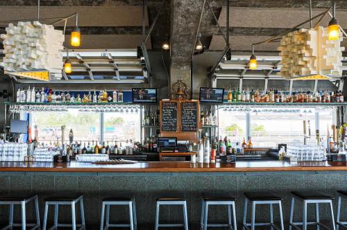 A modern bar with a long counter, shelves of liquor, and unique light fixtures, featuring large windows and stools.
