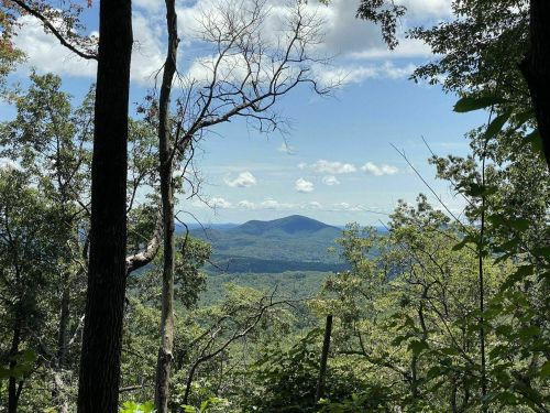 A scenic view of rolling hills and mountains framed by trees under a blue sky with scattered clouds.