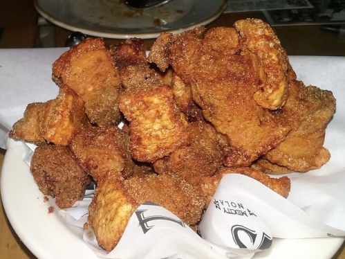 A plate of crispy, golden-brown fried pork belly pieces, served on a white paper lining.