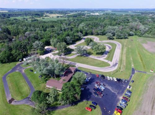 Aerial view of a racetrack surrounded by greenery, with a parking area and a building nearby.