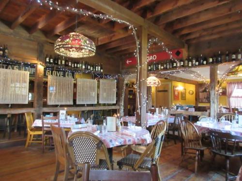 Cozy restaurant interior with wooden beams, tables set with checkered tablecloths, and warm lighting from hanging lamps.