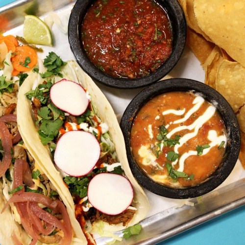 A platter with tacos topped with radishes and cilantro, accompanied by salsa, beans, and tortilla chips.