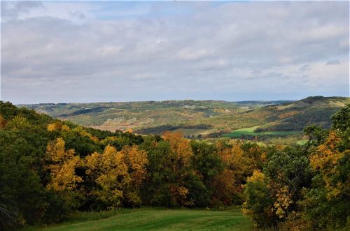 A scenic view of rolling hills covered in autumn foliage, with a cloudy sky above.