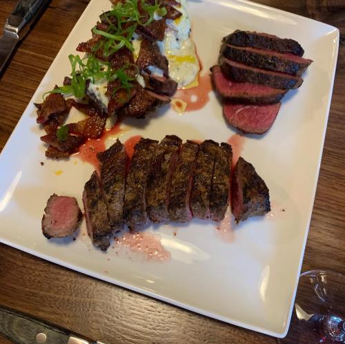 A plate featuring sliced steak, garnished with green onions, alongside a portion of meat with a crispy exterior.