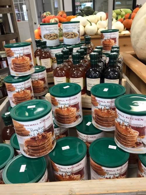 A display of canned pumpkin and syrup products in a market, with pumpkins and gourds in the background.