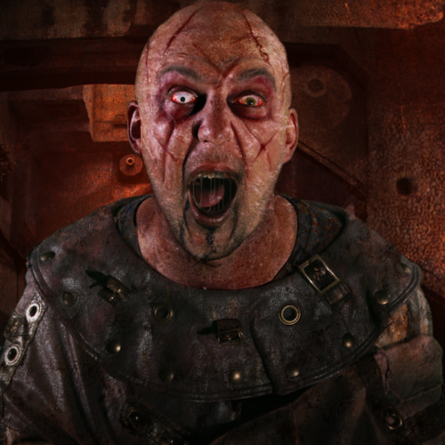 A bald, scarred man in a tattered outfit screams, with intense eyes and a distressed expression against a dark background.