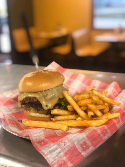 A cheeseburger with melted cheese and lettuce, served with a side of golden fries on a red-checkered paper.