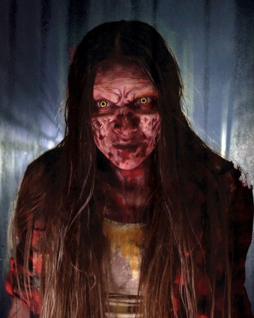 A terrifying figure with long hair, glowing yellow eyes, and a bloodied face, set against a dark, eerie background.