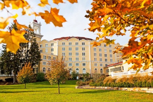 A historic yellow hotel surrounded by autumn foliage and green lawns under a clear sky.