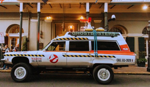A Ghostbusters-themed vehicle parked outside a building, featuring iconic logos and colorful decorations.