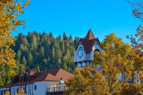 A charming building with a clock tower surrounded by autumn trees and a backdrop of green hills under a clear blue sky.