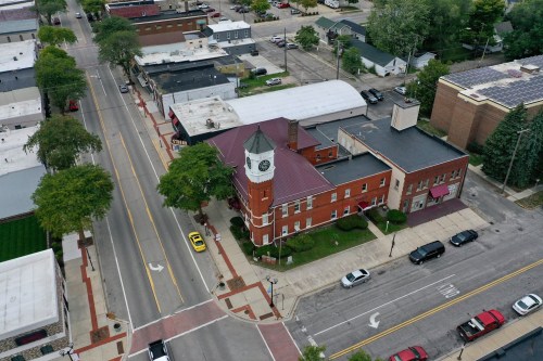 Aerial view of a town square featuring a clock tower, shops, and tree-lined streets.