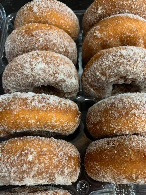 A close-up of sugar-coated donuts arranged in a clear plastic container.