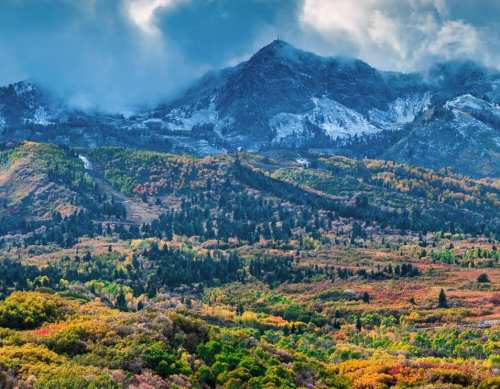 A scenic view of mountains with a mix of autumn foliage and patches of snow under a cloudy sky.