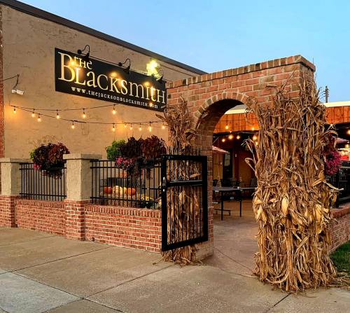 Entrance to The Blacksmith restaurant, featuring a brick archway adorned with corn stalks and vibrant flowers.