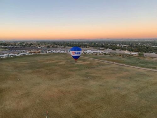 A colorful hot air balloon with a US Bank logo floats above a grassy field at sunrise, with a distant landscape.