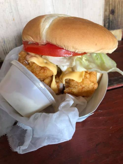 A fried chicken sandwich with lettuce, tomato, and cheese, served with a small cup of sauce on the side.