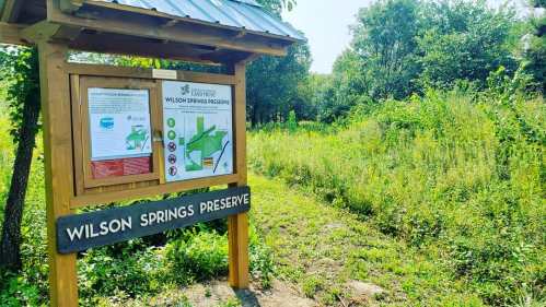 Sign for Wilson Springs Preserve with maps and information, surrounded by lush greenery and trees.