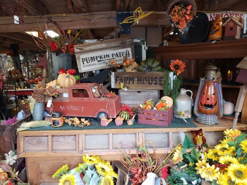 A rustic market display featuring pumpkins, autumn decor, and a vintage red truck with a "Market" sign.