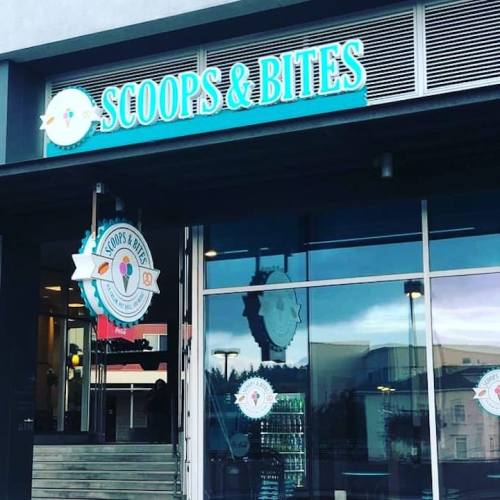 Sign for "Scoops & Bites" ice cream shop, featuring a colorful logo and large windows.