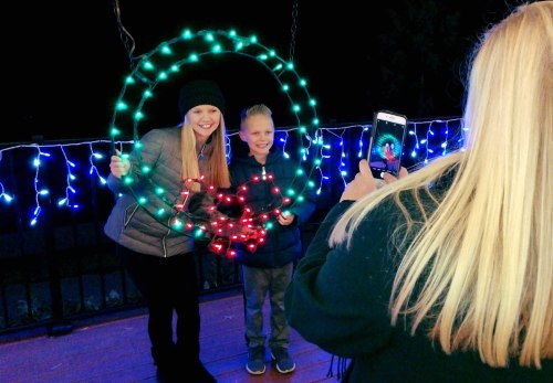 A woman and a boy pose with a lit wreath while another person takes their photo in front of colorful lights.