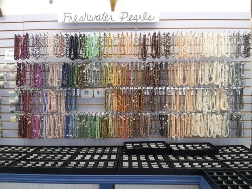 A display of colorful freshwater pearl strands arranged on a wall, with black boxes underneath for additional items.