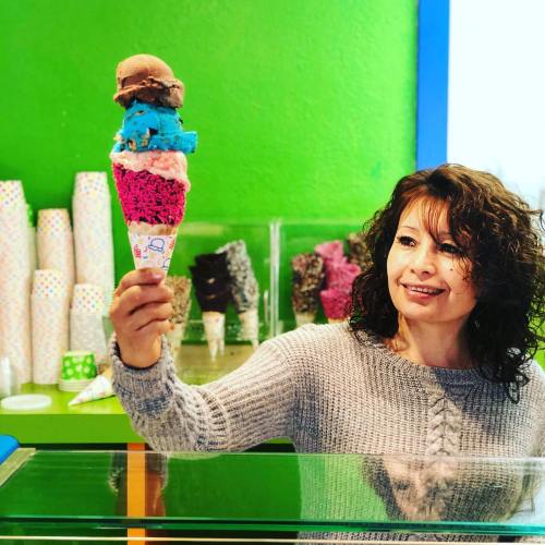 A woman holds a colorful ice cream cone with multiple scoops in a vibrant ice cream shop.