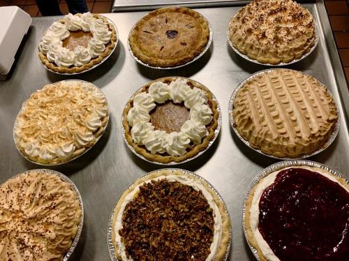 A variety of delicious pies on a metal table, featuring whipped cream, nuts, and fruit toppings.