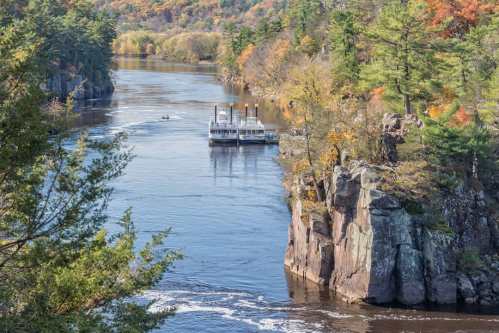 A river flows past rocky cliffs, with a boat navigating the water surrounded by autumn foliage.