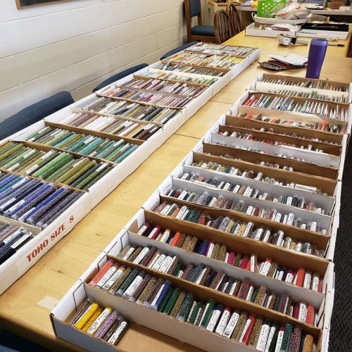 A table displaying organized boxes of colorful beads in various sizes and shades, neatly arranged for crafting.