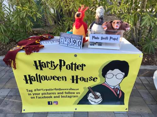 A table with a Harry Potter-themed banner, props, and a sign for a photo booth at a Halloween event.