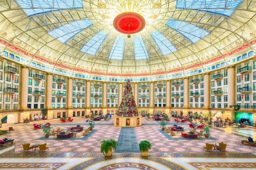 A grand hotel lobby with a high glass dome, featuring a large Christmas tree and elegant seating areas.