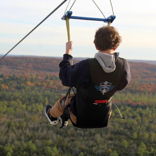 A person zip-lining over a forested landscape with autumn colors in the trees.