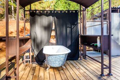 Outdoor bathing area featuring a vintage bathtub, wooden deck, and black curtains for privacy.
