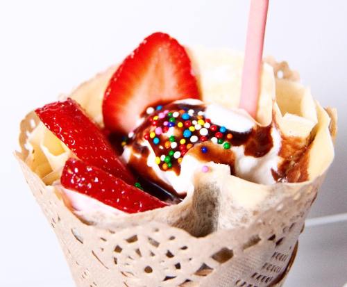A dessert cup with ice cream, chocolate sauce, sprinkles, and fresh strawberries in a decorative waffle cone.