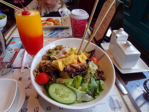A colorful salad with greens, cherry tomatoes, and chicken, accompanied by a vibrant drink and a cup of coffee.