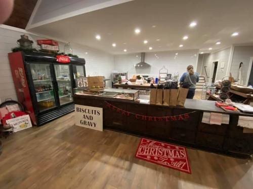 A cozy restaurant interior decorated for Christmas, featuring a counter with bags, a fridge, and festive signs.