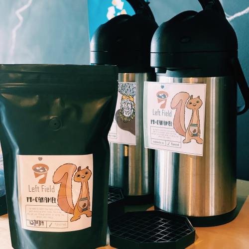 A bag of PB-Caramel coffee next to two metal coffee dispensers, all featuring a squirrel logo.