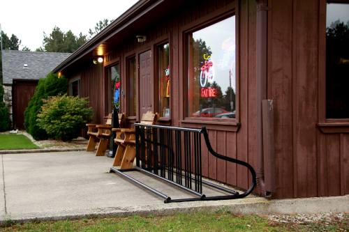 A wooden building with large windows, featuring a bike rack and outdoor seating on a concrete path.