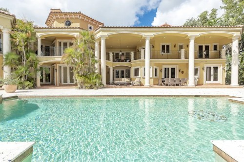 Luxurious villa with a pool, surrounded by palm trees and featuring multiple balconies under a blue sky.