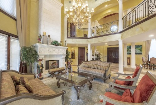 Luxurious living room with high ceilings, elegant furniture, a chandelier, and a fireplace, featuring warm colors and decor.