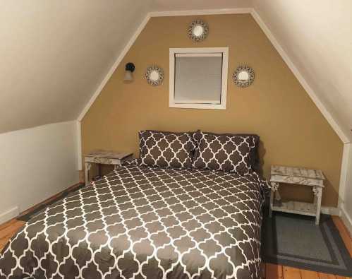 Cozy attic bedroom with a patterned bedspread, two side tables, and decorative mirrors on the wall.